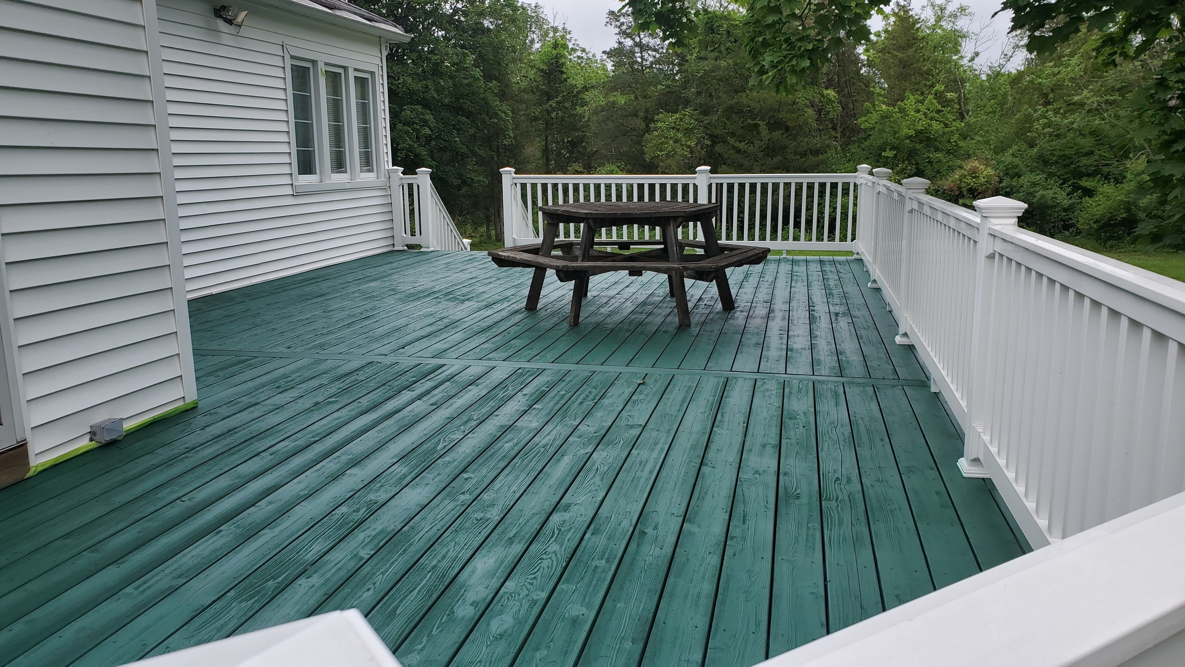 Residential deck freshly stained in rich teal green color with white vinyl railing and patio furniture
