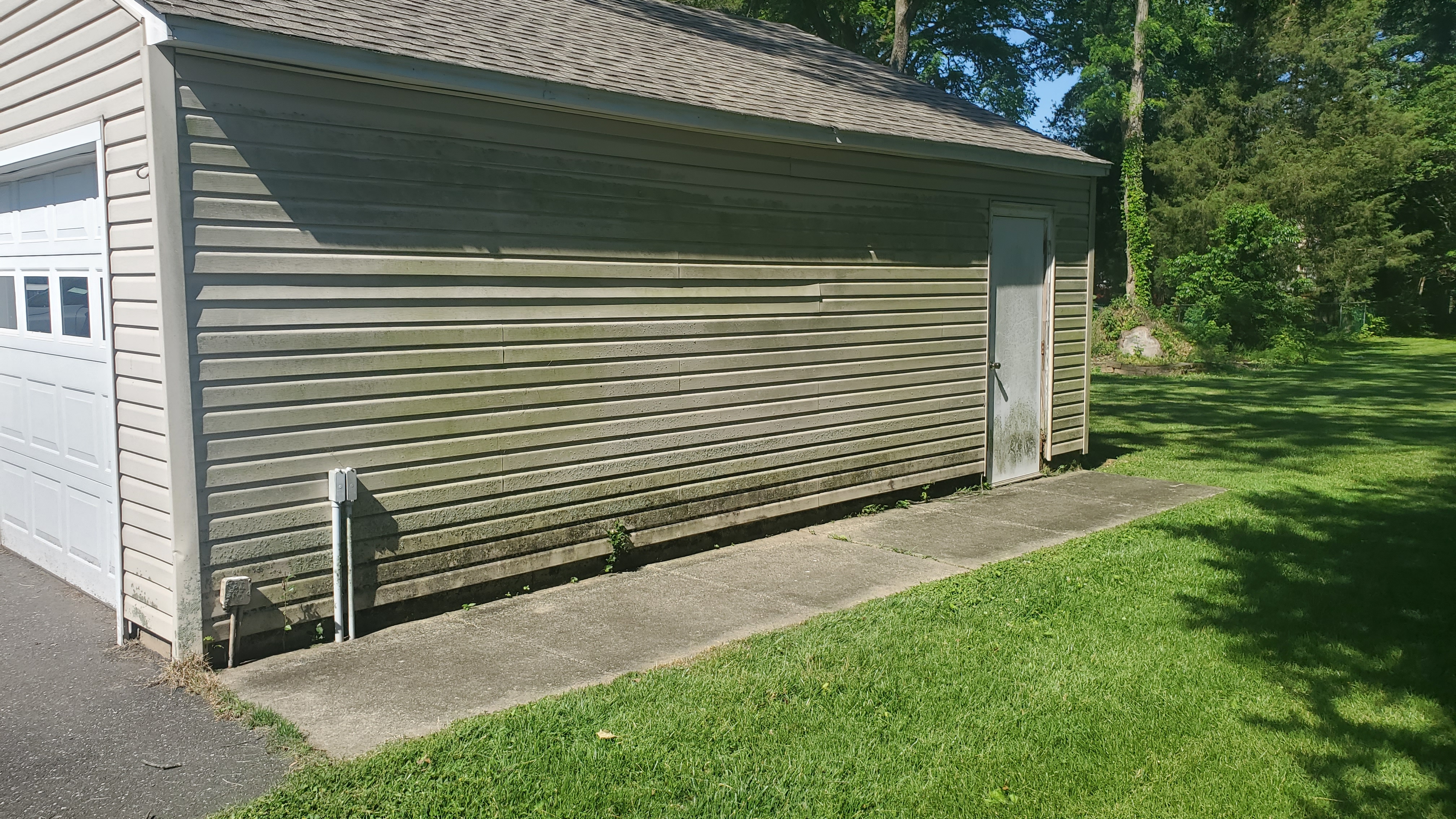 Garage building exterior with heavy green algae staining on siding before cleaning