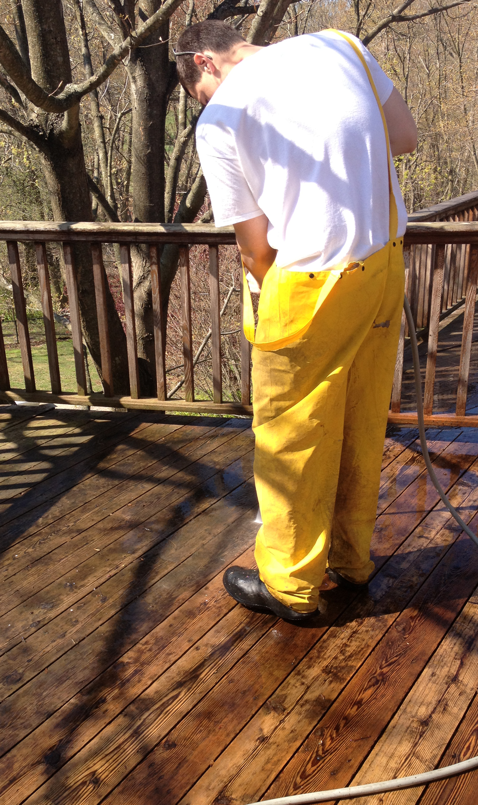 Technician in blue shirt using pressure washer to clean weathered wood deck railing