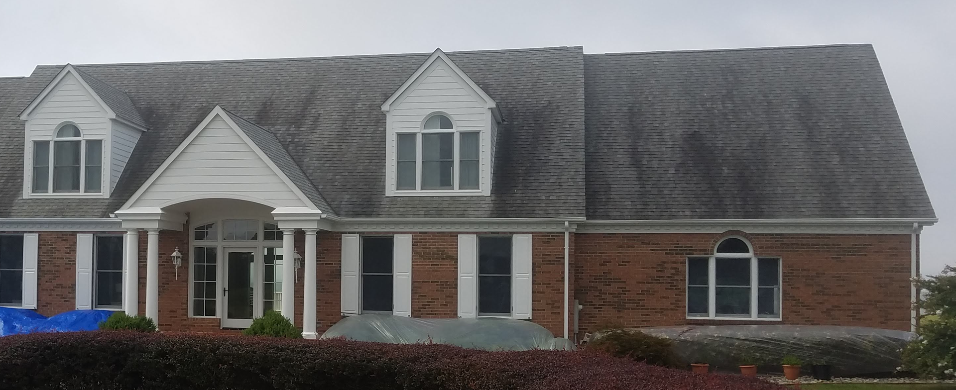 Large two story brick colonial home with severe black algae streaks across entire roof