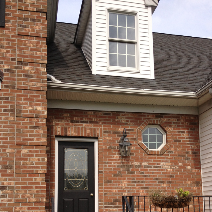 Clean brick home with dark shingles after professional roof soft wash treatment showing fully restored appearance
